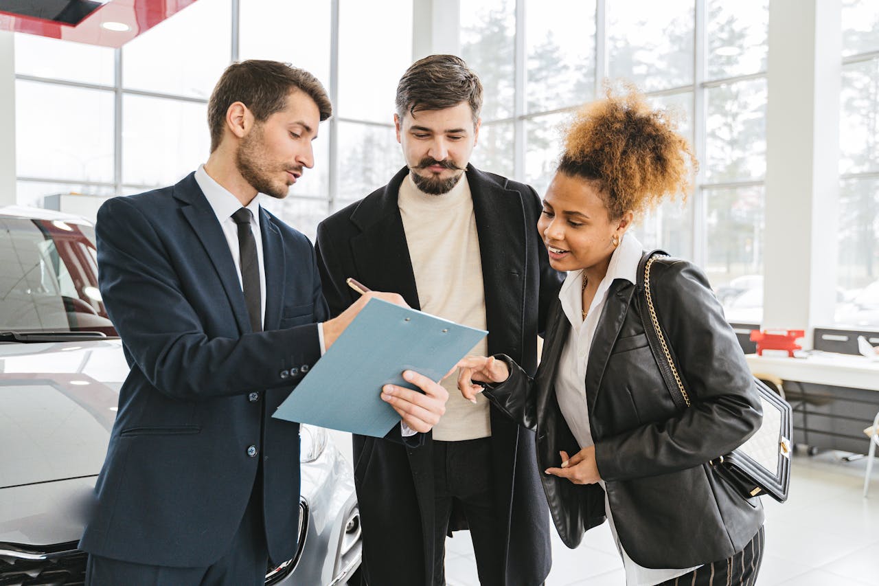 Three business professionals discussing car purchase details inside a modern dealership.