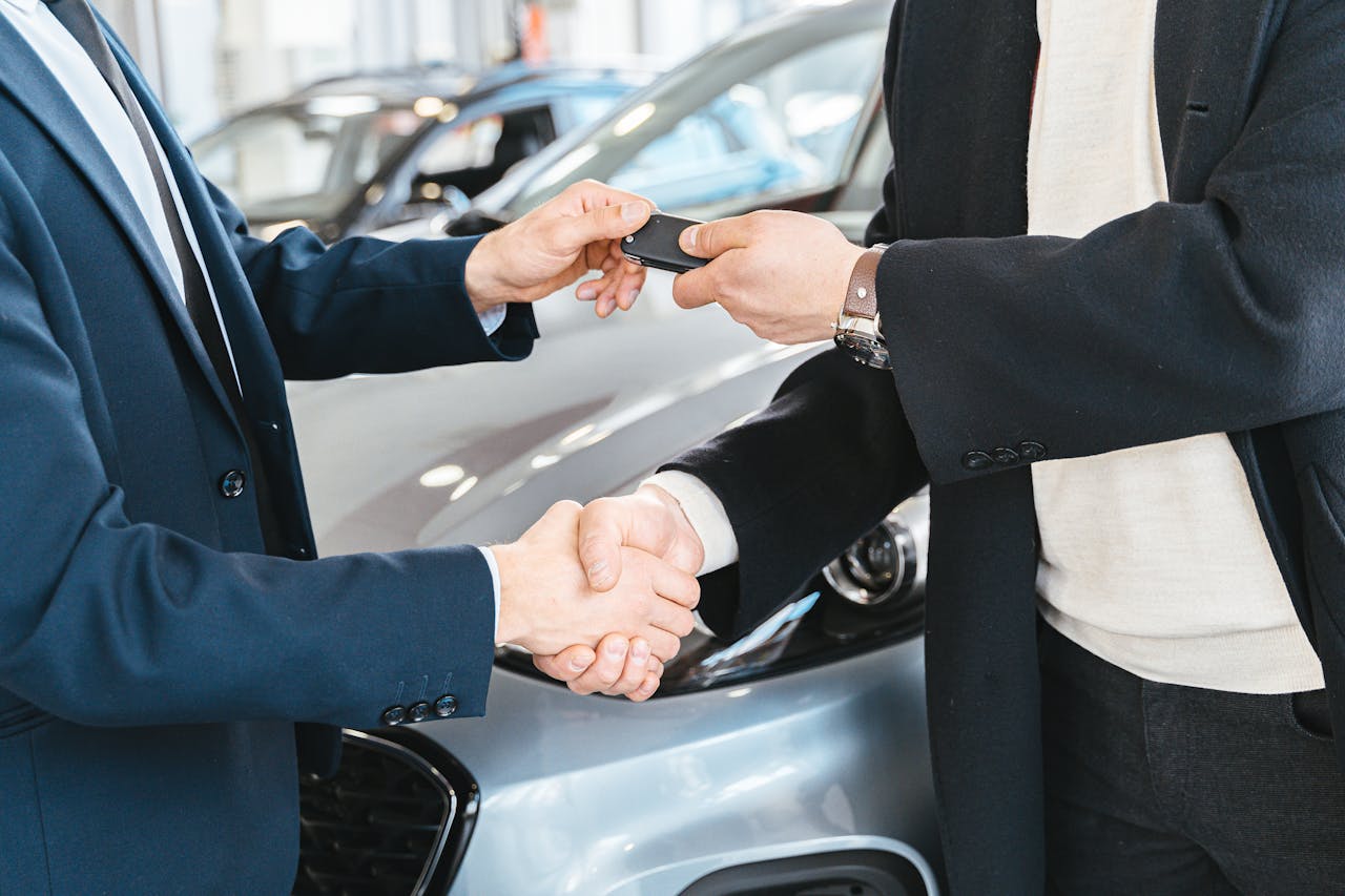 services-02 Two businessmen shaking hands and exchanging car keys in a dealership. Symbolizes a successful deal.